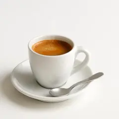 Tazzina di caffè espresso su piattino bianco con cucchiaino. Un piacere quotidiano, ma attenzione al caffè e colesterolo.