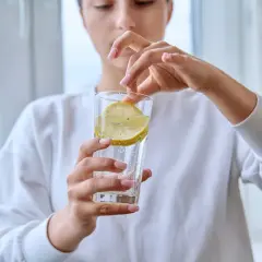 Donna aggiunge una fetta di limone in un bicchiere d'acqua frizzante. Attenzione, acqua e limone fa male al fegato se consumata in eccesso.
