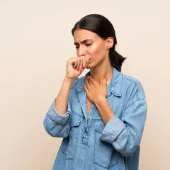 Donna con la mano sulla bocca e l'altra sul petto, soffre di tosse da reflusso.