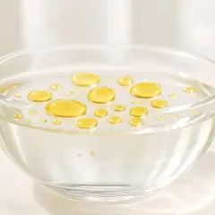 Gocce dorate di olio feci che galleggiano sulla superficie di un liquido trasparente in una ciotola di vetro.
