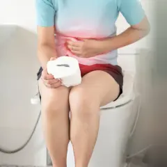 Persona con dolori addominali, seduta sul water con rotolo di carta igienica. Forse la mozzarella ha causato la diarrea.