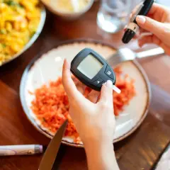 Mani che usano glucometro e lancetta. Piatto con carote grattugiate. Cosa non mangiare la sera prima delle analisi del sangue.