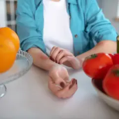 Donna si gratta il braccio arrossato, circondata da frutta e verdura, suggerendo una dieta disintossicante per orticaria.
