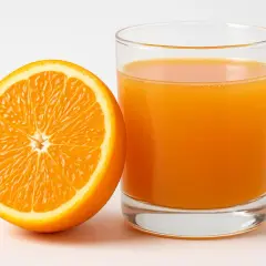 Mezza arancia succosa accanto a un bicchiere di succo d'arancia. Un'immagine che fa pensare alle arance e alla glicemia.