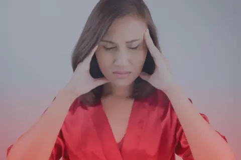 Donna con le mani sulle tempie, espressione sofferente, forse un sintomo di carenza di ferro al viso.
