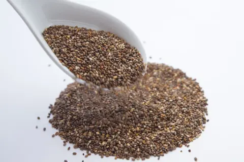 Un cucchiaio bianco versa semi di chia, piccoli alleati per sgonfiare la pancia.