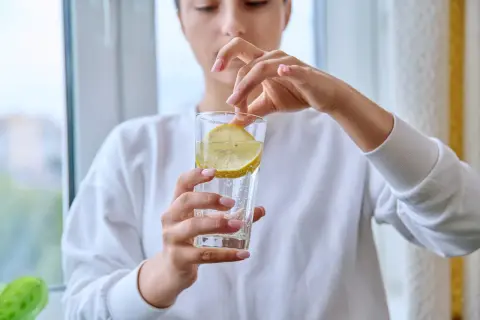 Donna aggiunge una fetta di limone in un bicchiere d'acqua frizzante. Attenzione, acqua e limone fa male al fegato se consumata in eccesso.