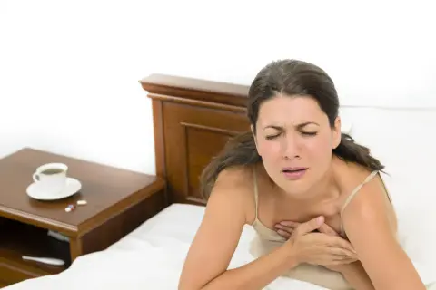 Donna si sveglia di soprassalto con tachicardia, stringendosi il petto. Sul comodino, caffè e pillole.
