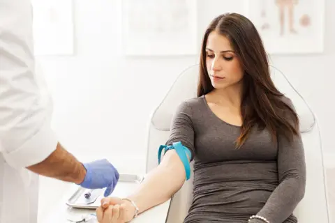 Donna in sala d'attesa per un prelievo di sangue. Il medico prepara l'ago per controllare la transaminasi GPT-ALT 57.