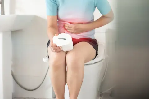 Persona con dolori addominali, seduta sul water con rotolo di carta igienica. Forse la mozzarella ha causato la diarrea.