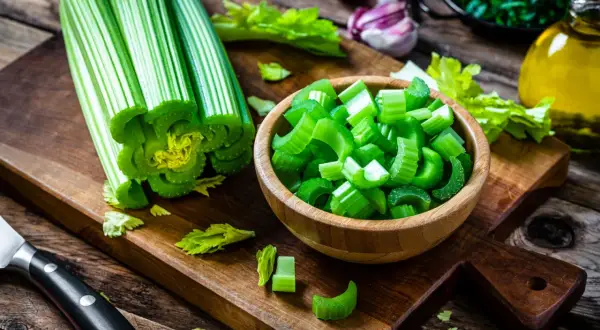Sedano fresco, tagliato e intero, pronto per essere gustato come verdure che non gonfiano la pancia. Sullo sfondo, aglio, erbe e olio d'oliva.