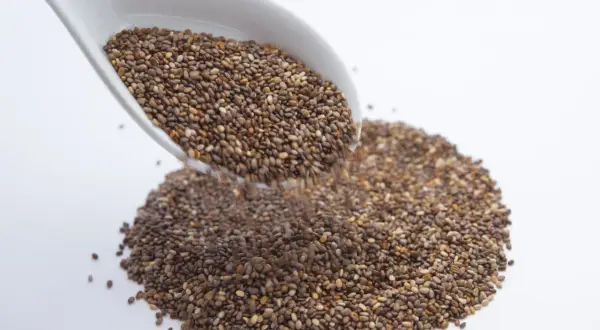 Un cucchiaio bianco versa semi di chia, piccoli alleati per sgonfiare la pancia.