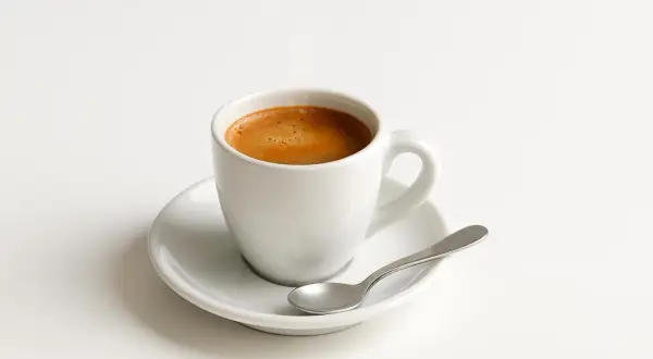 Tazzina di caffè espresso su piattino bianco con cucchiaino. Un piacere quotidiano, ma attenzione al caffè e colesterolo.