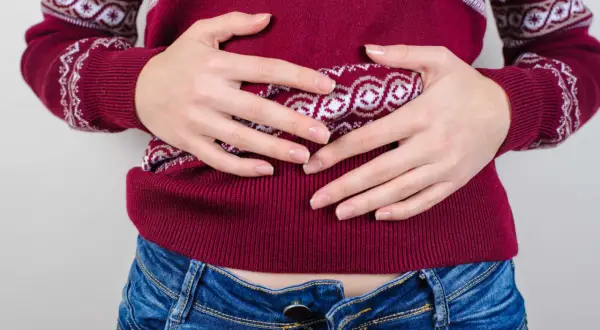 Mani che stringono l'addome, con un maglione bordeaux e jeans. Ho mangiato troppo, mi sento male.