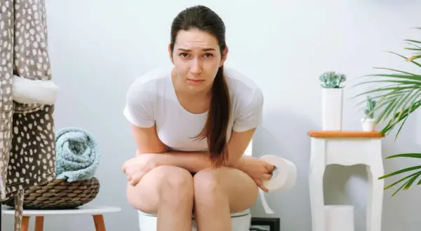 Donna sul water con espressione preoccupata, pensando a cosa mangiare per il fecaloma.
