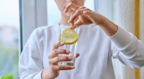 Donna aggiunge una fetta di limone in un bicchiere d'acqua frizzante. Attenzione, acqua e limone fa male al fegato se consumata in eccesso.