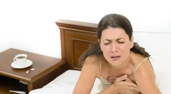 Donna si sveglia di soprassalto con tachicardia, stringendosi il petto. Sul comodino, caffè e pillole.