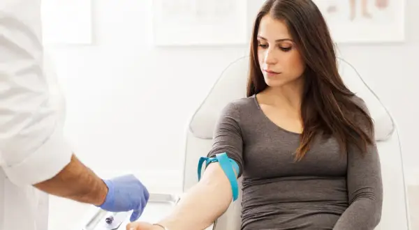 Donna in sala d'attesa per un prelievo di sangue. Il medico prepara l'ago per controllare la transaminasi GPT-ALT 57.