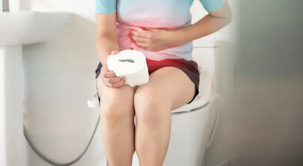 Persona con dolori addominali, seduta sul water con rotolo di carta igienica. Forse la mozzarella ha causato la diarrea.