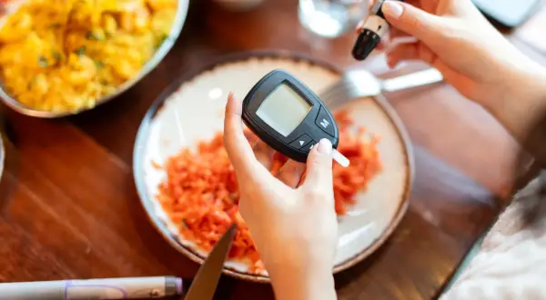 Mani che usano glucometro e lancetta. Piatto con carote grattugiate. Cosa non mangiare la sera prima delle analisi del sangue.