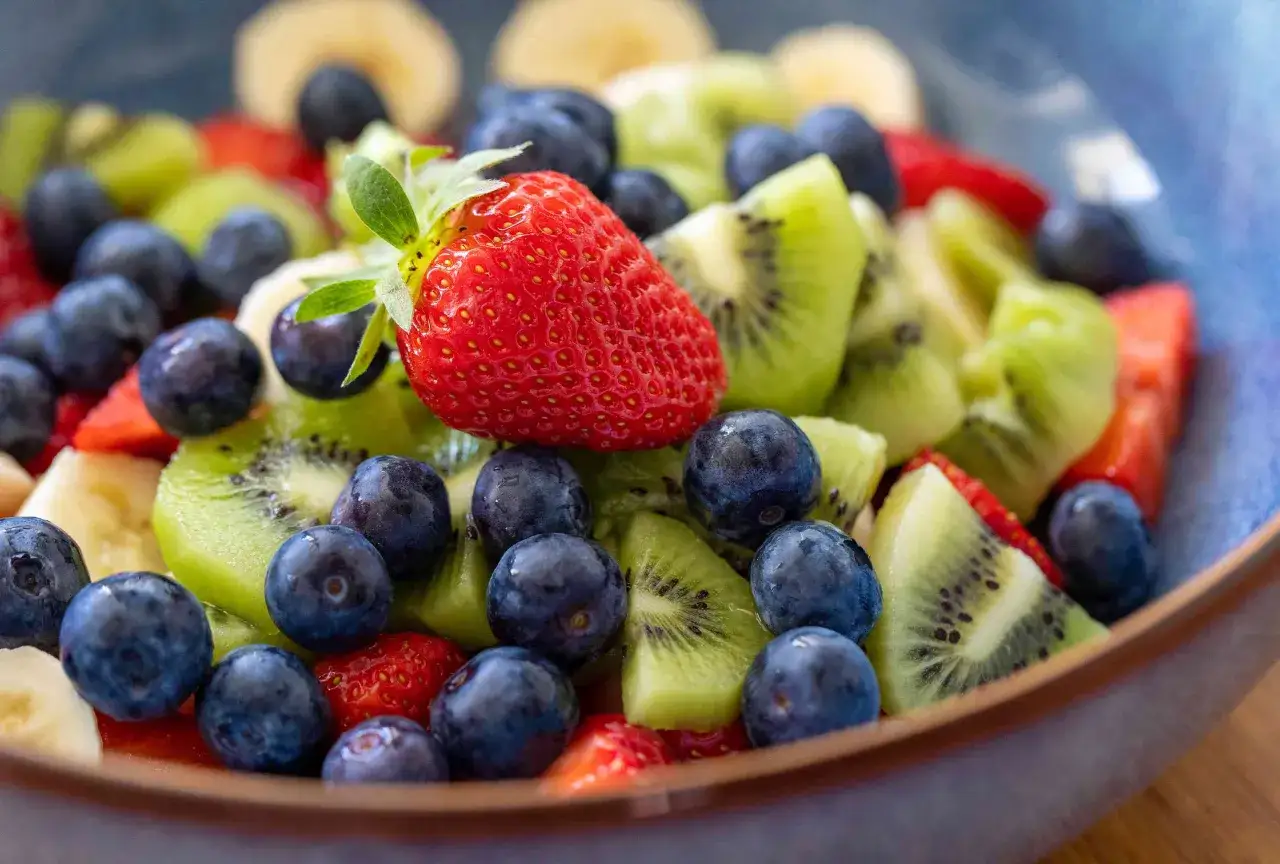 Un primo piano di una ciotola piena di frutta fresca: fragole, mirtilli, kiwi e banane. Chi dice che la frutta fa ingrassare?