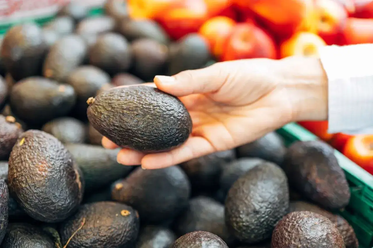 Mano che sceglie un avocado, un frutto amico per la glicemia. Frutta fresca in primo piano.