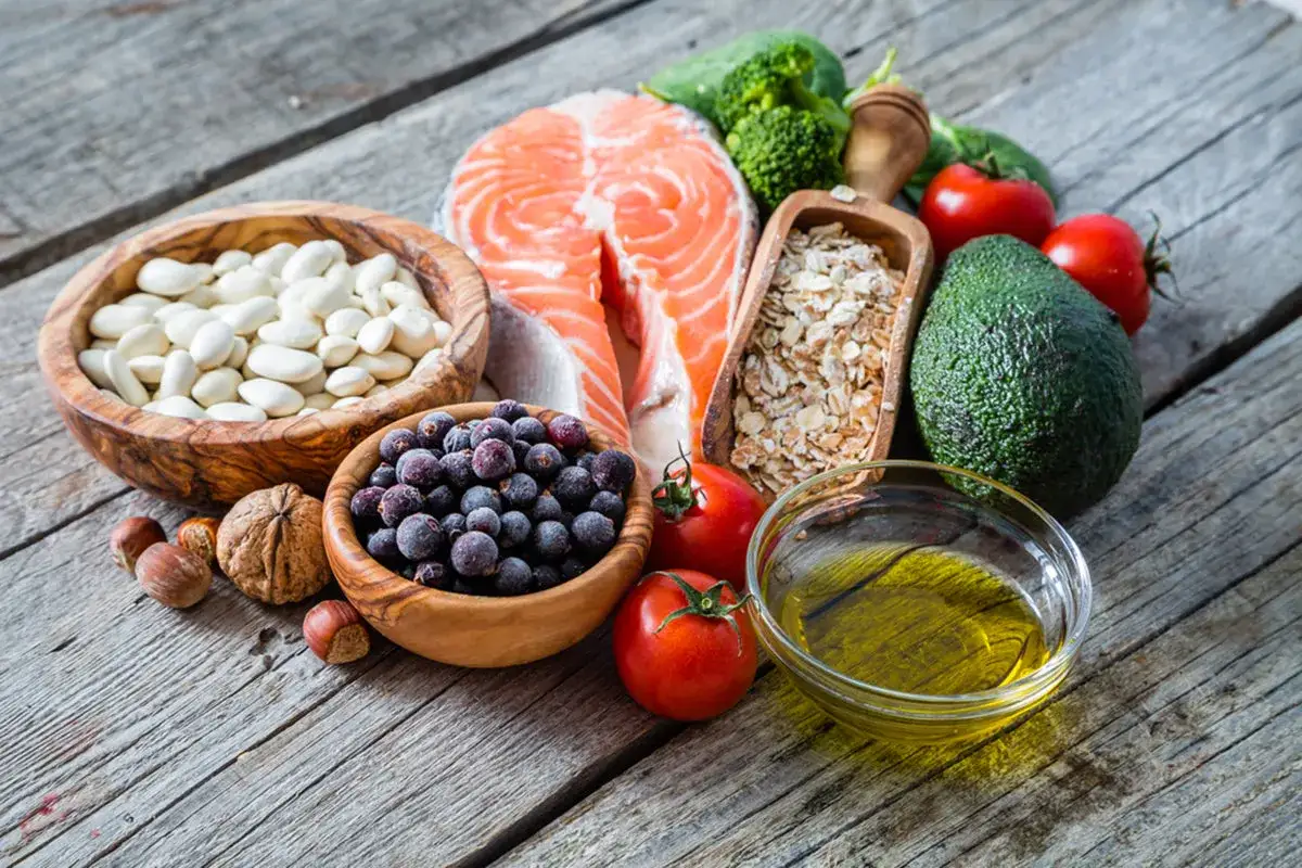 Ingredienti per una dieta colesterolo alto donna menopausa: salmone, fagioli, frutti di bosco, avvocato, fiocchi d'avena, pomodori, olio d'oliva.