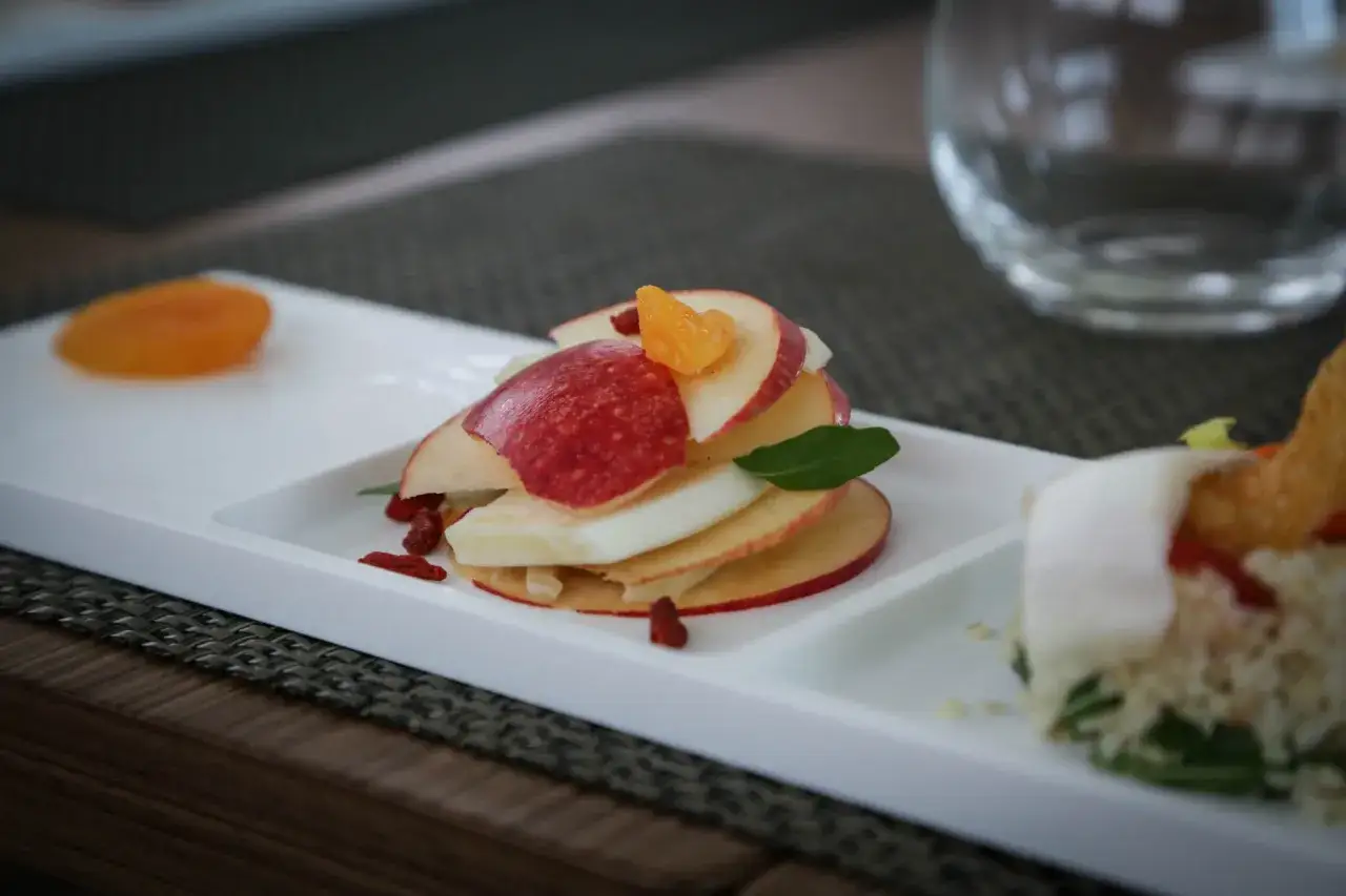 Delizioso dessert di frutta dopo i pasti: fettine di mela rosse e bianche alternate, con bacche di goji e un tocco di mandarino.