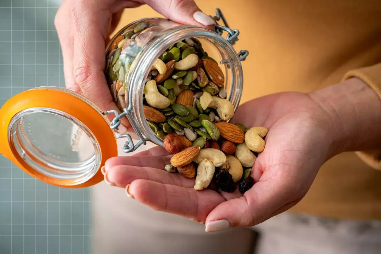Mani versano un mix di frutta secca e semi da un barattolo. Un'ottima fonte di nutrienti, la frutta secca e il colesterolo possono coesistere in una dieta equilibrata.