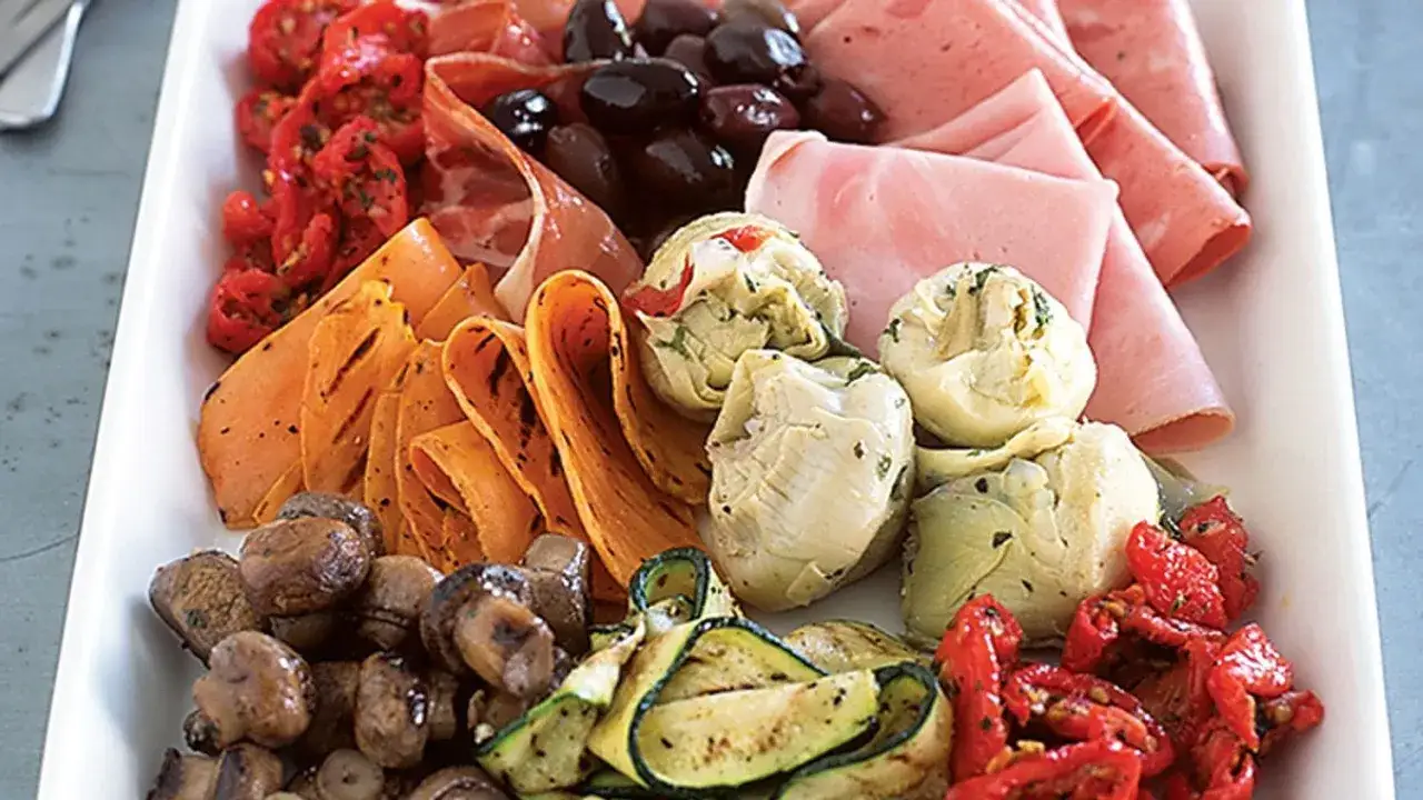 Piatto ricco con salumi, pomodorini secchi, olive, carciofini, funghi e zucchine grigliate, perfetto per una dieta low carb.