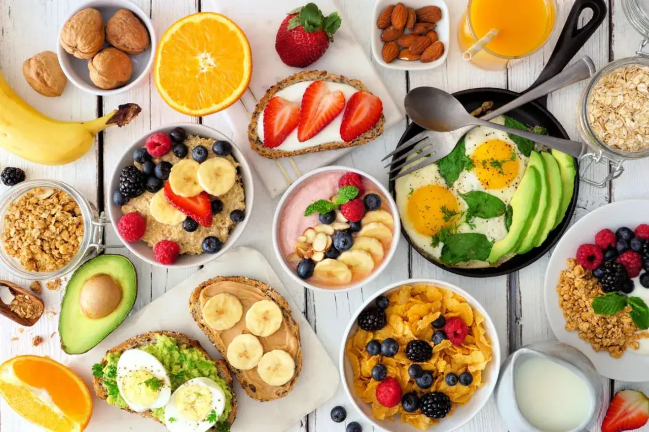 Un tavolo pieno di opzioni per una colazione a basso indice glicemico: porridge, uova, avocado toast, frutta fresca e cereali.