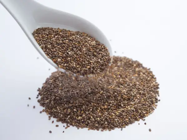 Un cucchiaio bianco versa semi di chia, piccoli alleati per sgonfiare la pancia.