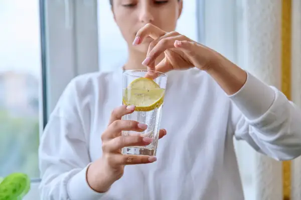 Donna aggiunge una fetta di limone in un bicchiere d'acqua frizzante. Attenzione, acqua e limone fa male al fegato se consumata in eccesso.